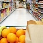 Grocery cart loaded with fresh fruit and bread moving through the aisle.