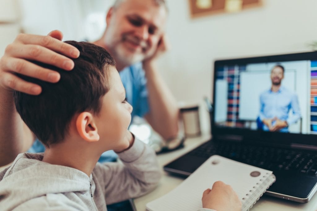 Studente in didattica a distanza. Il padre aiuta suo figlio con i compiti a casa. Ragazzo in videoconferenza con l'insegnante sul portatile a casa.
