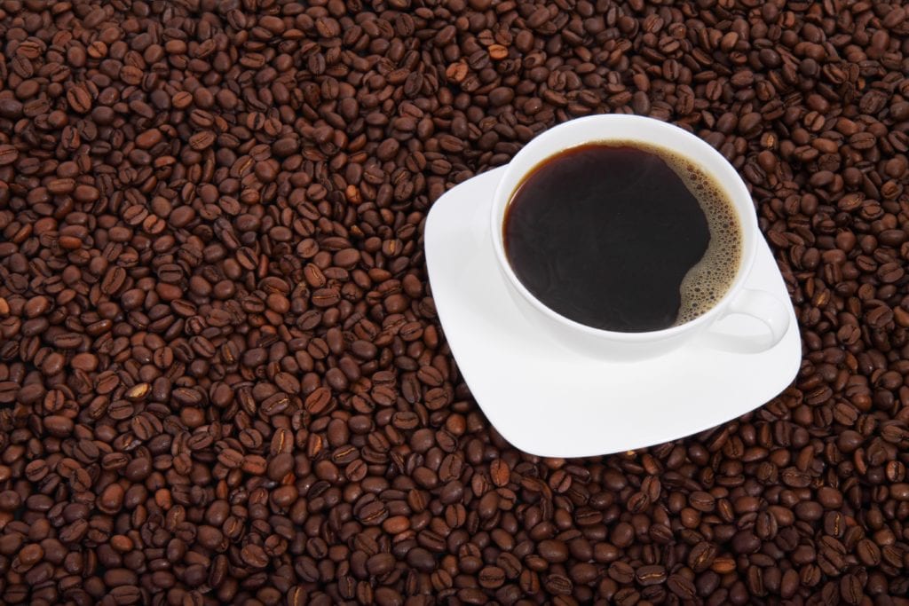 Il caffè come alleato della melanina contro il melanoma. Tazza di caffè posata sui chicchi