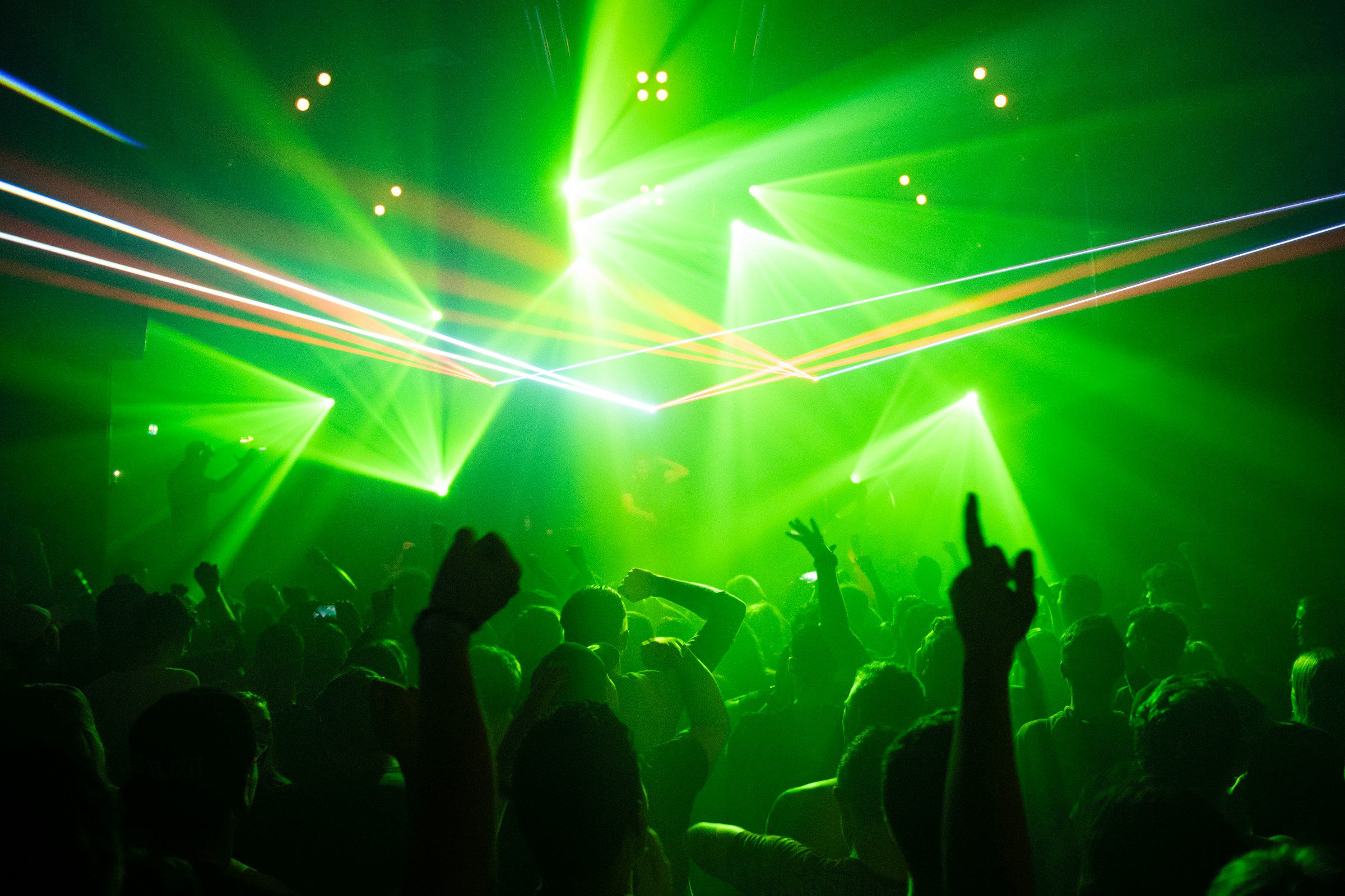"Musica techno". Gente balla in discoteca sollevando mani in aria, avvolti da luce verde.