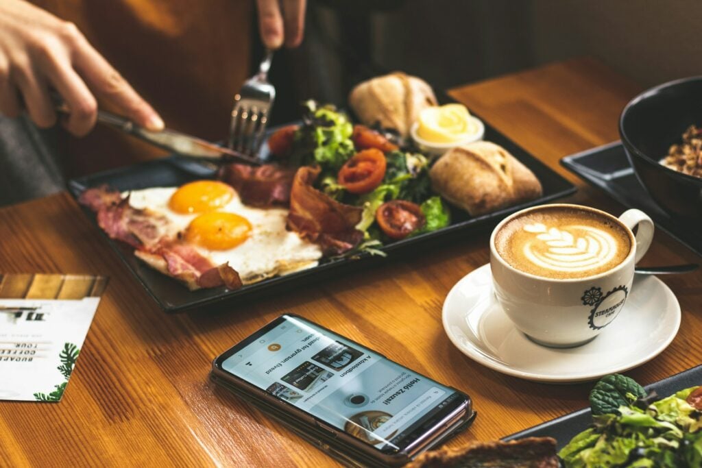 "Spreco alimentare" uomo al tavolo con la colazione servita e un'app per il cibo nel telefono