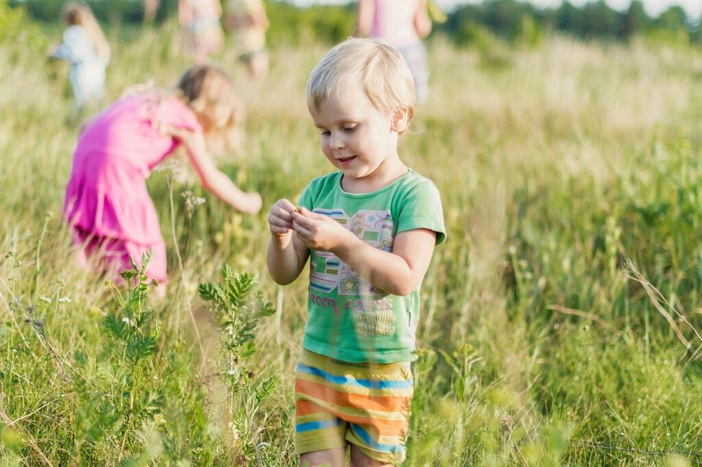Bambini e natura: crescita equilibrata tra gioco e apprendimento. Un bambino in età prescolare gioca sorridente in un prato