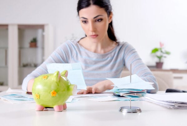 budget personale e pianificazione finanziaria: in primo piano una donna seduta alla scrivania a conteggiare le spese. Di fronte un salvadanaio.