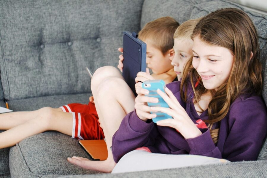 tre bambini seduti sul divano con i loro dispositivi digitali