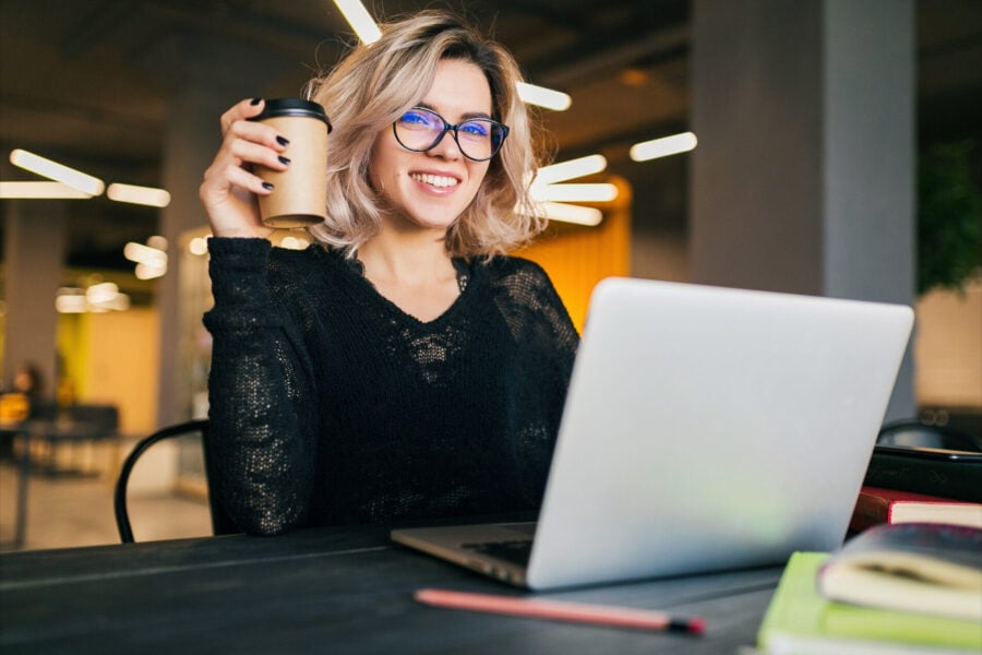 settimana lavorativa corta: donna bionda, con un caff&egrave; in mano, sorridente al computer
