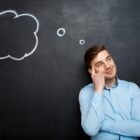 Pensiero laterale: uomo che pensa con il dito sulla tempia, davanti ad una lavagna con le nuvolette dei pensieri