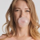 Masticare chewing gum: ragazza bionda che soffia divertita per fare una bolla con la gomma da masticare